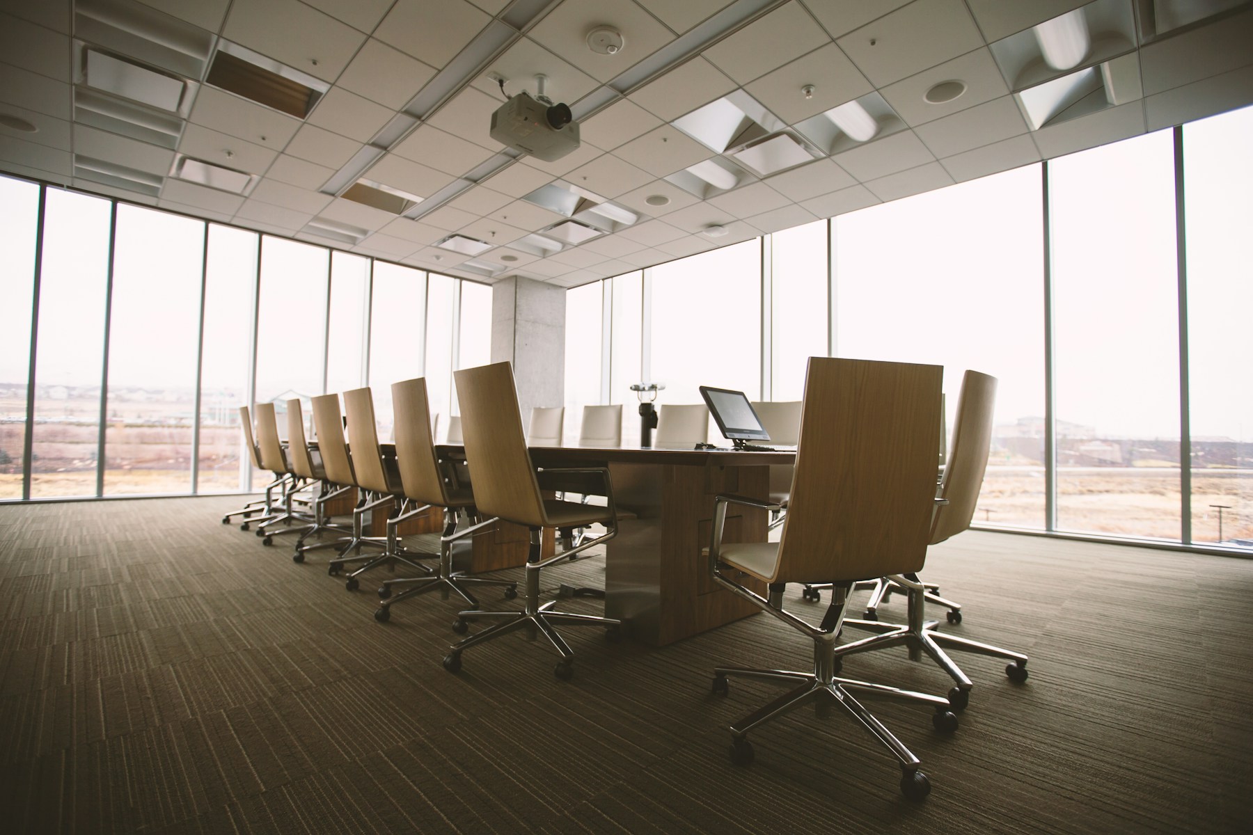 A formal boardroom with a long wooden conference table, executive chairs, and floor-to-ceiling windows.